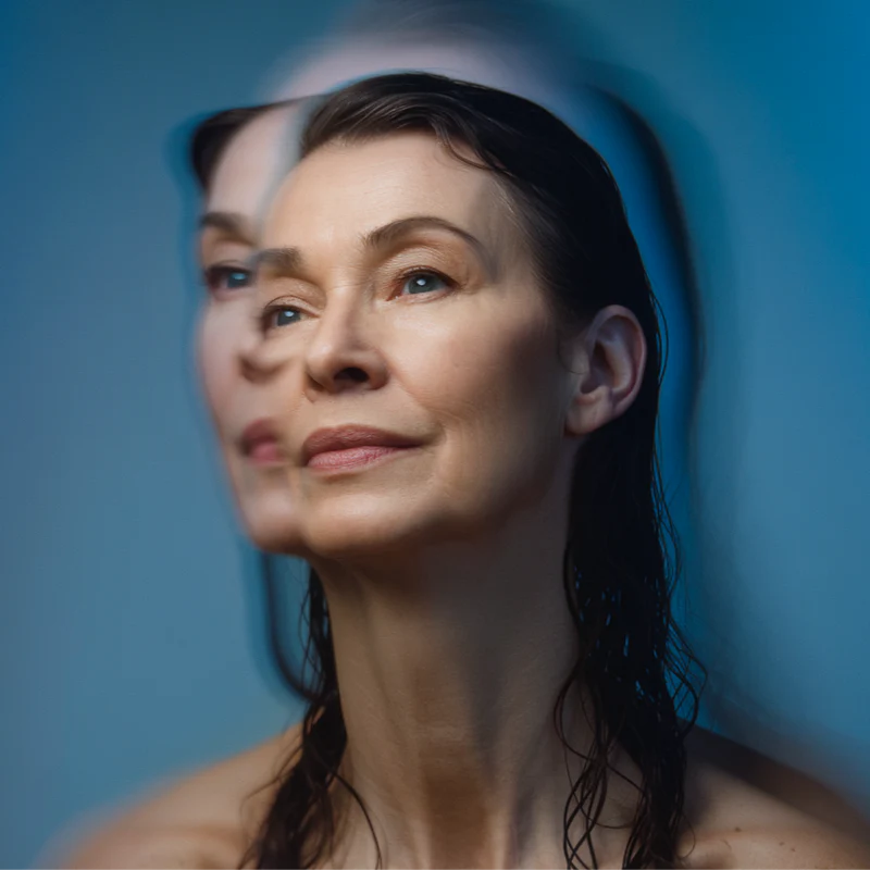 Portrait of a woman lit against a blue background, a second exposure layered behind her